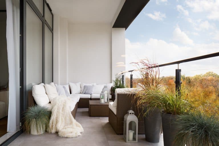 a cozy balcony with a glass railing and decorated with furniture and a white throw